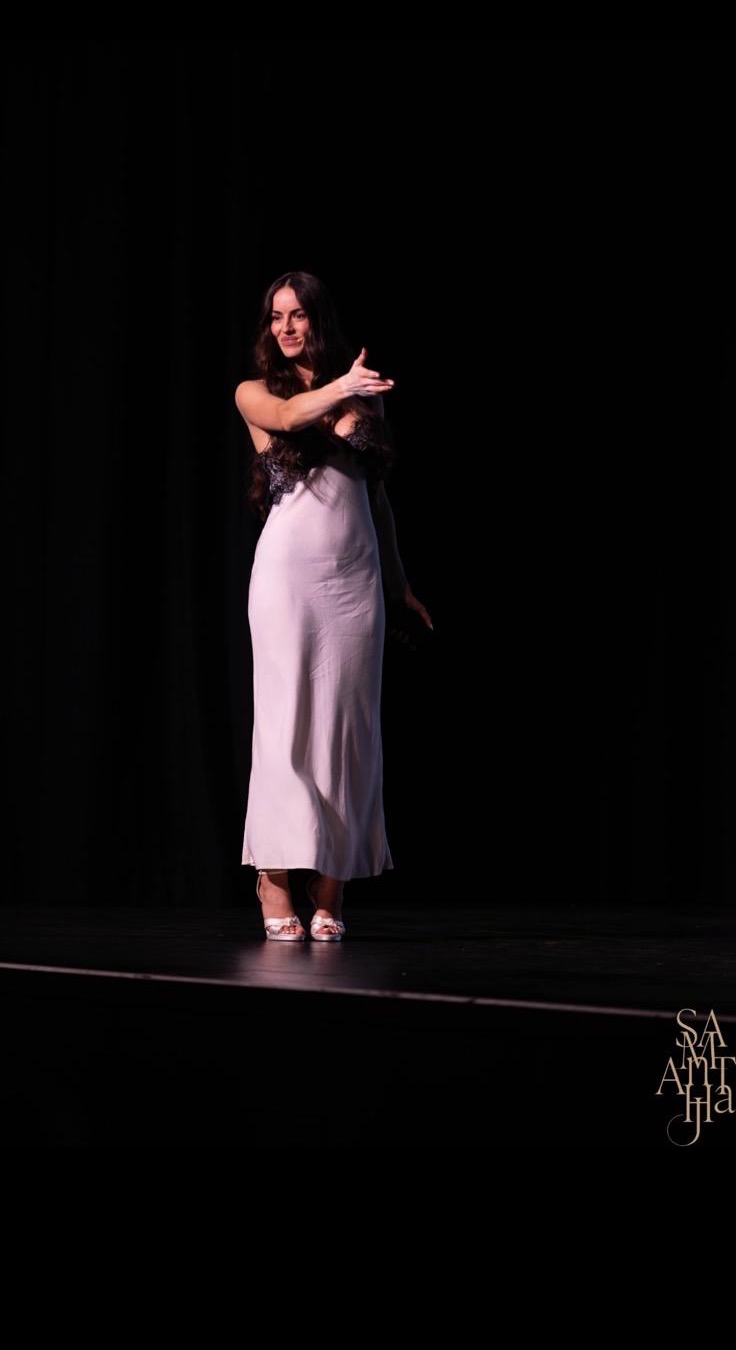 Tijana on stage in a long ivory dress, gesturing to the audience